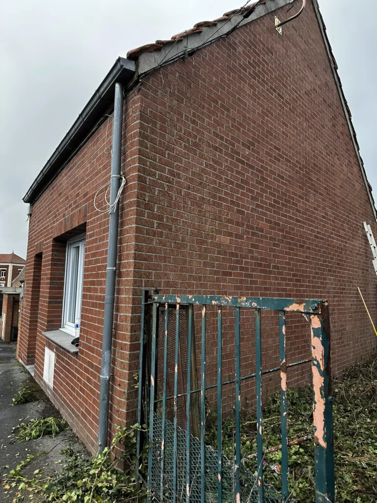 Façade en brique rouge d'un petit bâtiment avec portail vert oxydé et gouttière