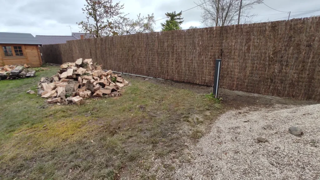 Tas de bois coupé stocké dans une cour fermée par une clôture en branches tressées